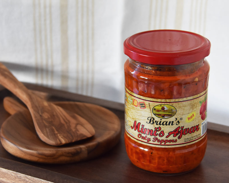 Jar of Brian's Minit' Ajour hot pepper sauce on a wooden tray with a wooden spoon.