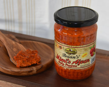 Jar of 'Brian's Mild Ajvar' on a wooden surface with a spoonful of ajvar.