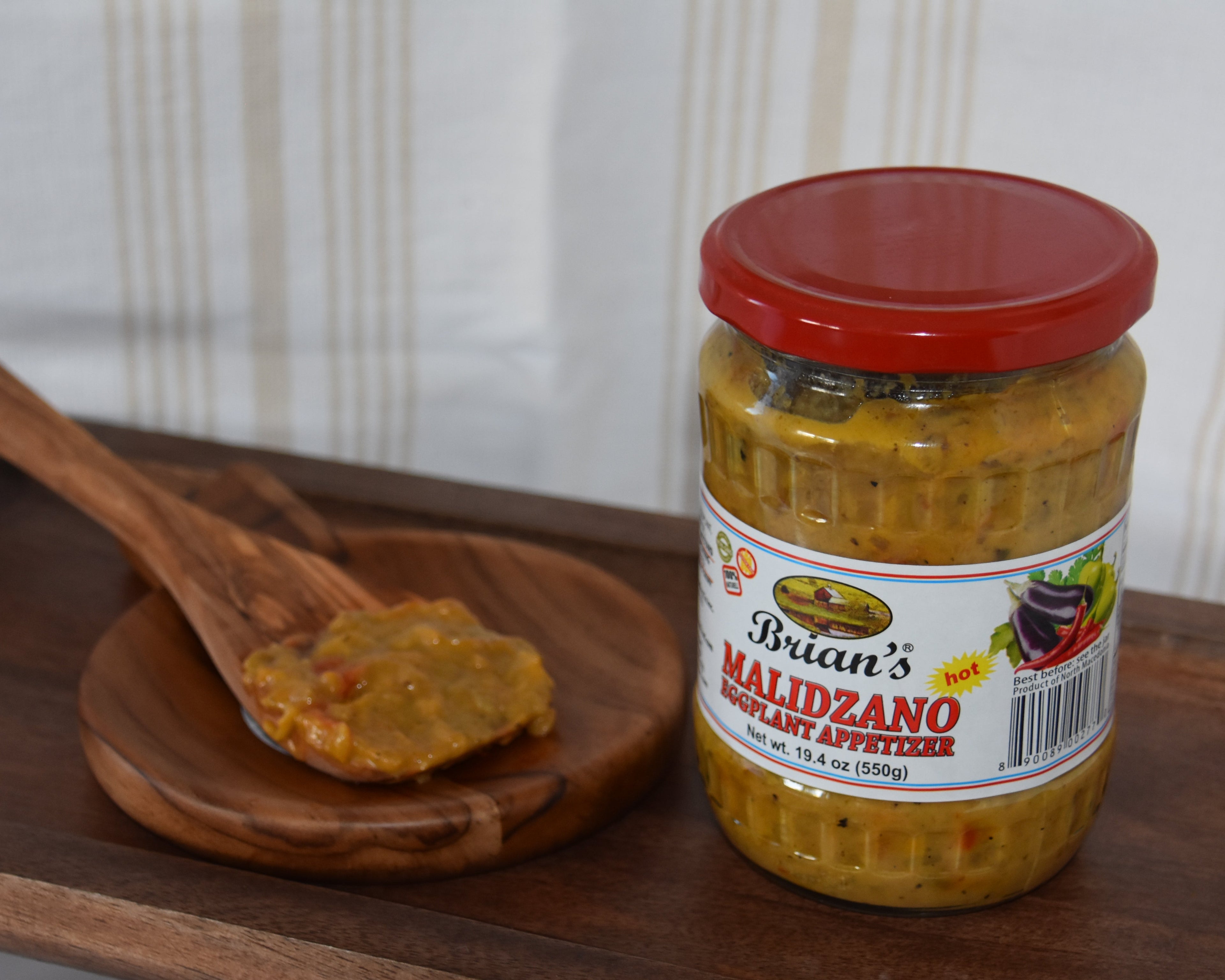 Jar of Brian's Maridzano hot pepper jelly on a wooden tray with a wooden spoon.