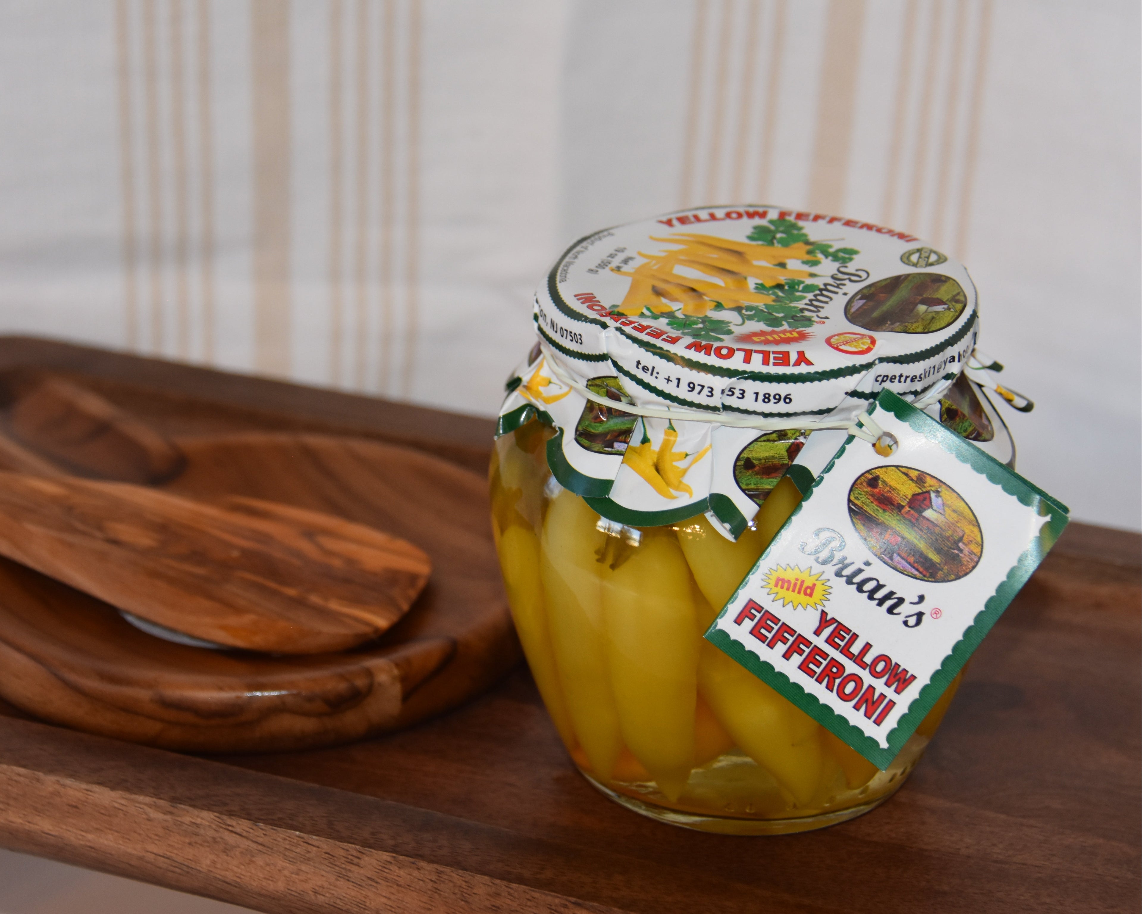 Jar of yellow pepperoni on a wooden tray with a striped background
