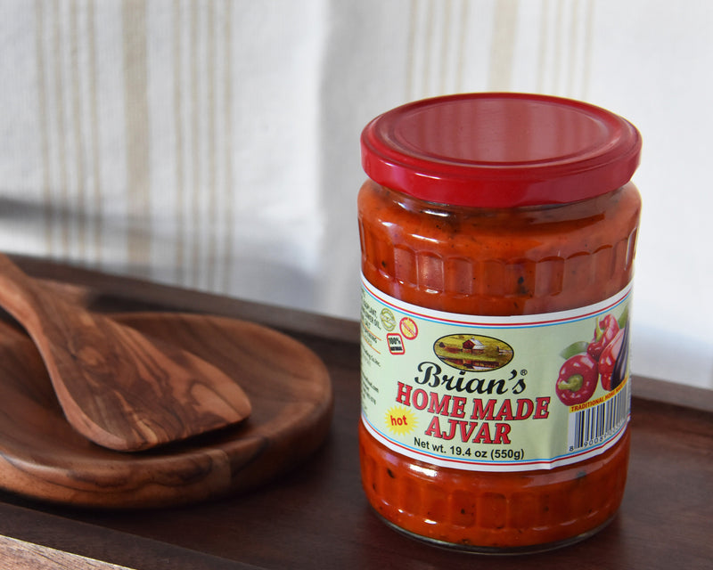 Jar of 'Brian's Home Made Ajvar' on a wooden tray with wooden spoons.