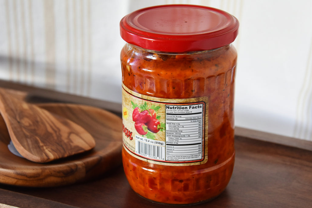 Jar of ajvar sauce with a red lid on a wooden surface.