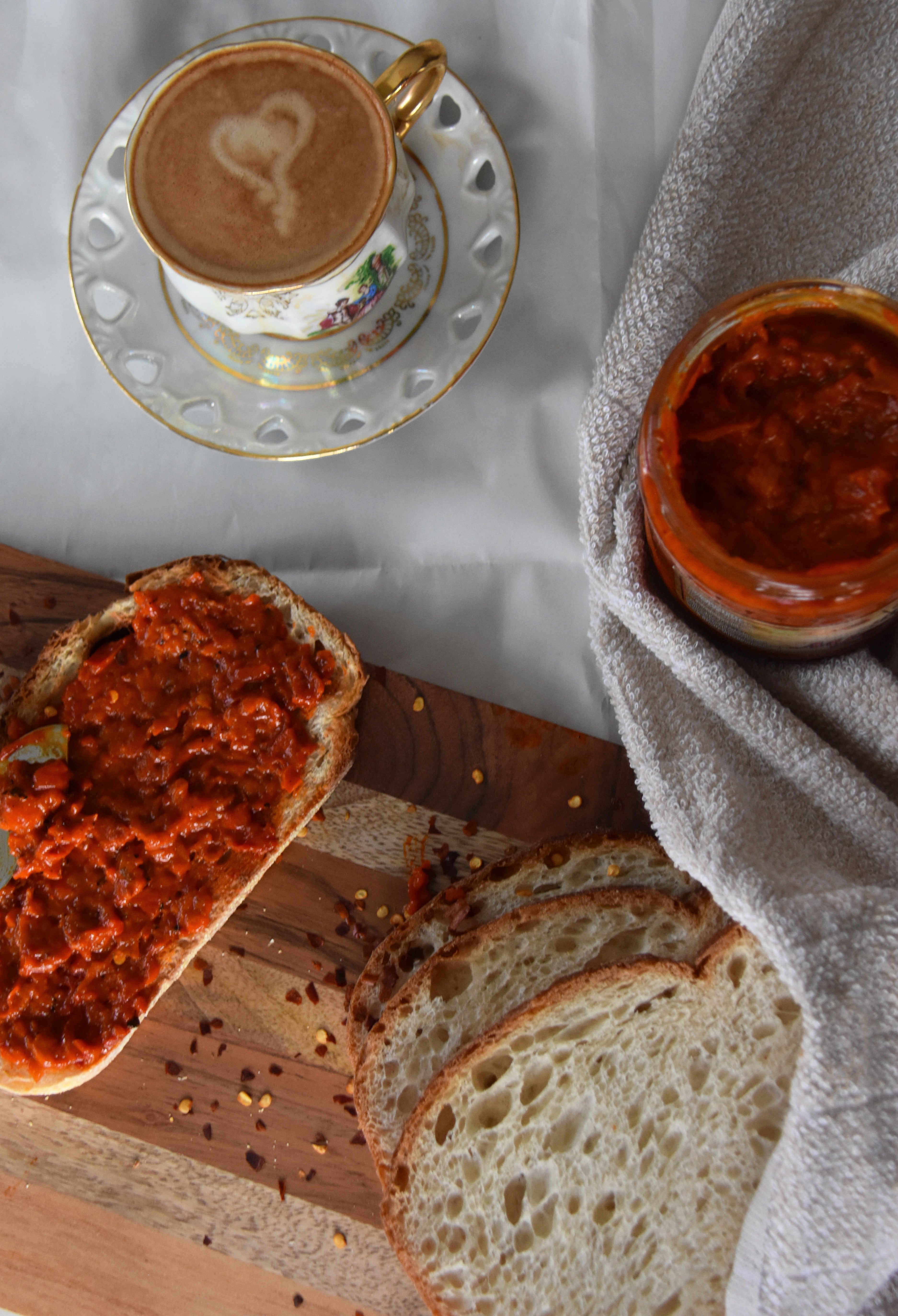 Breakfast scene with coffee, bread, and a jar of red spread on a white tablecloth.